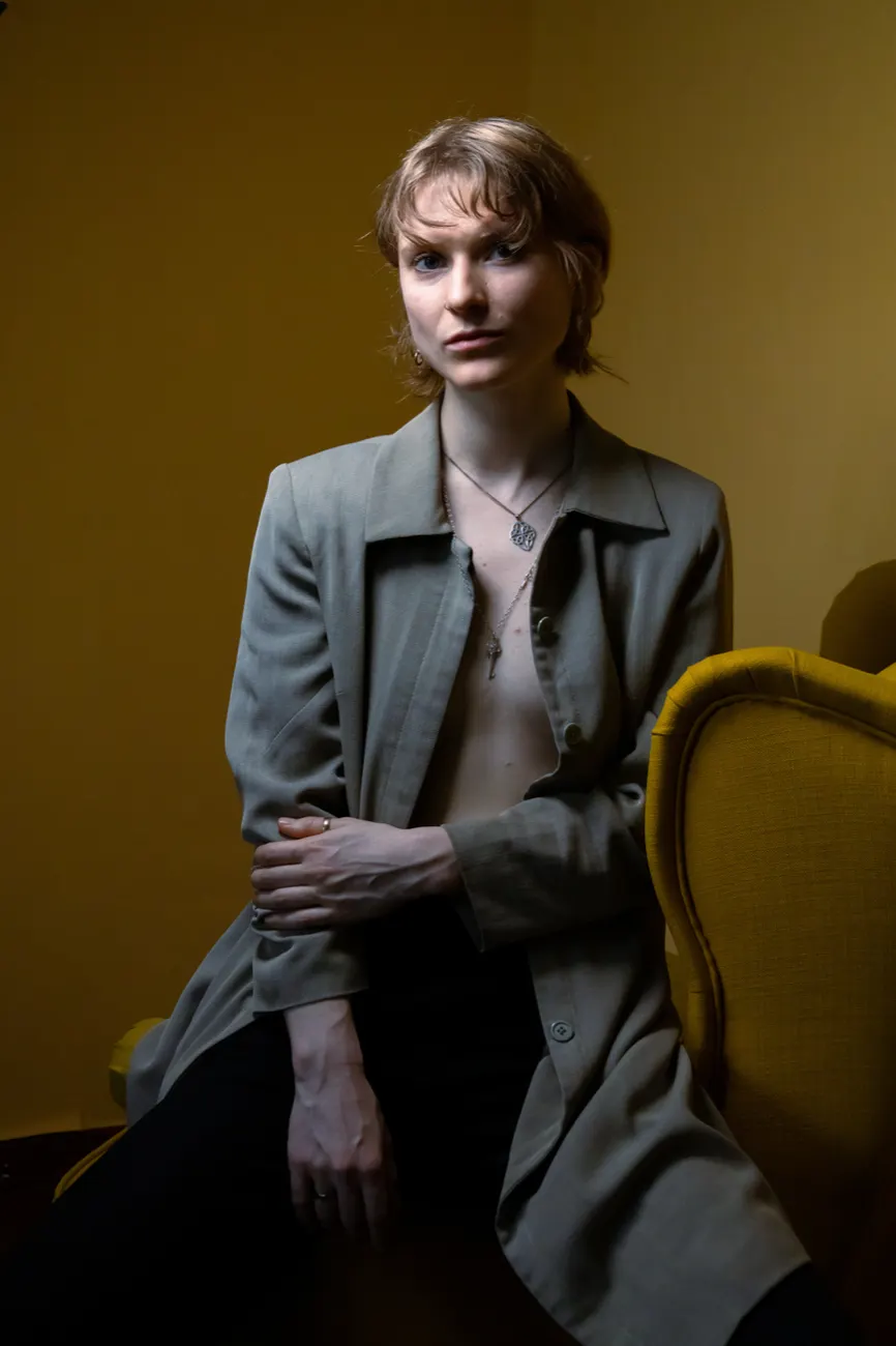 Eva in a grey blazer beside a yellow armchair
