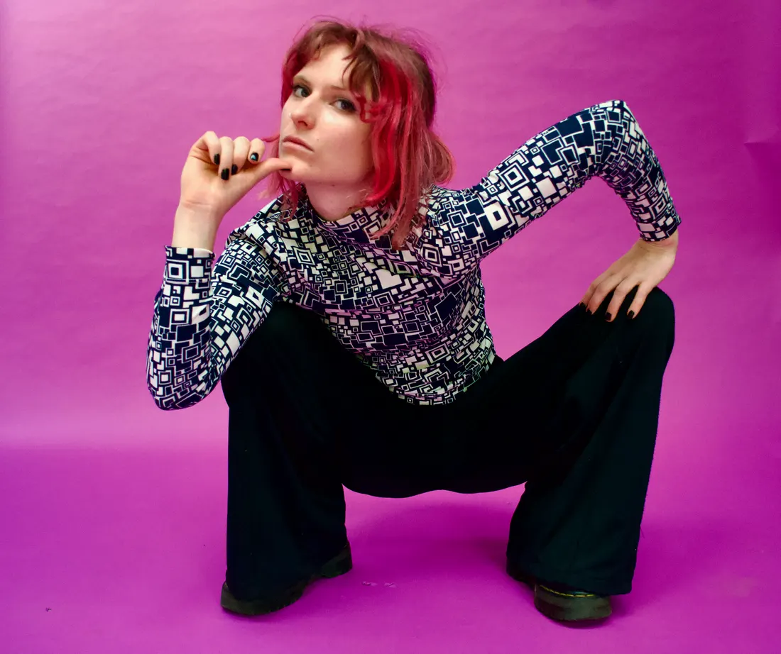 Eva crouching against a magenta backdrop, chin on her hand