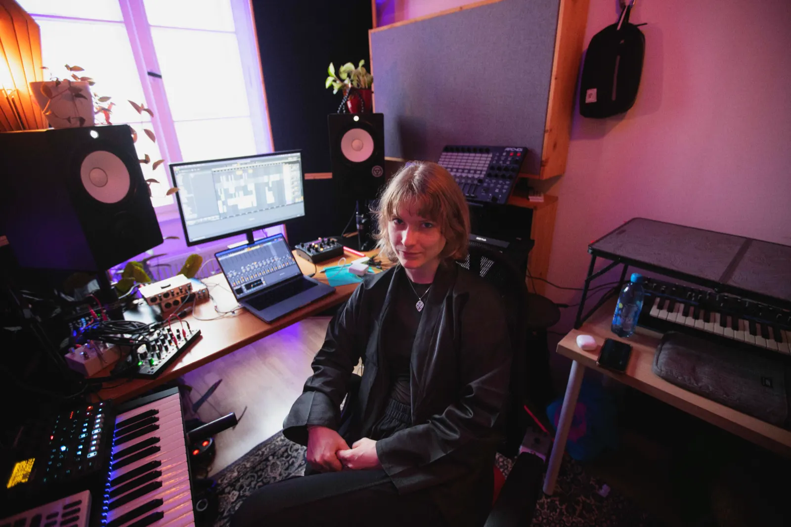 Eva at her studio desk in pink light, monitors, synths and an Ableton session around her