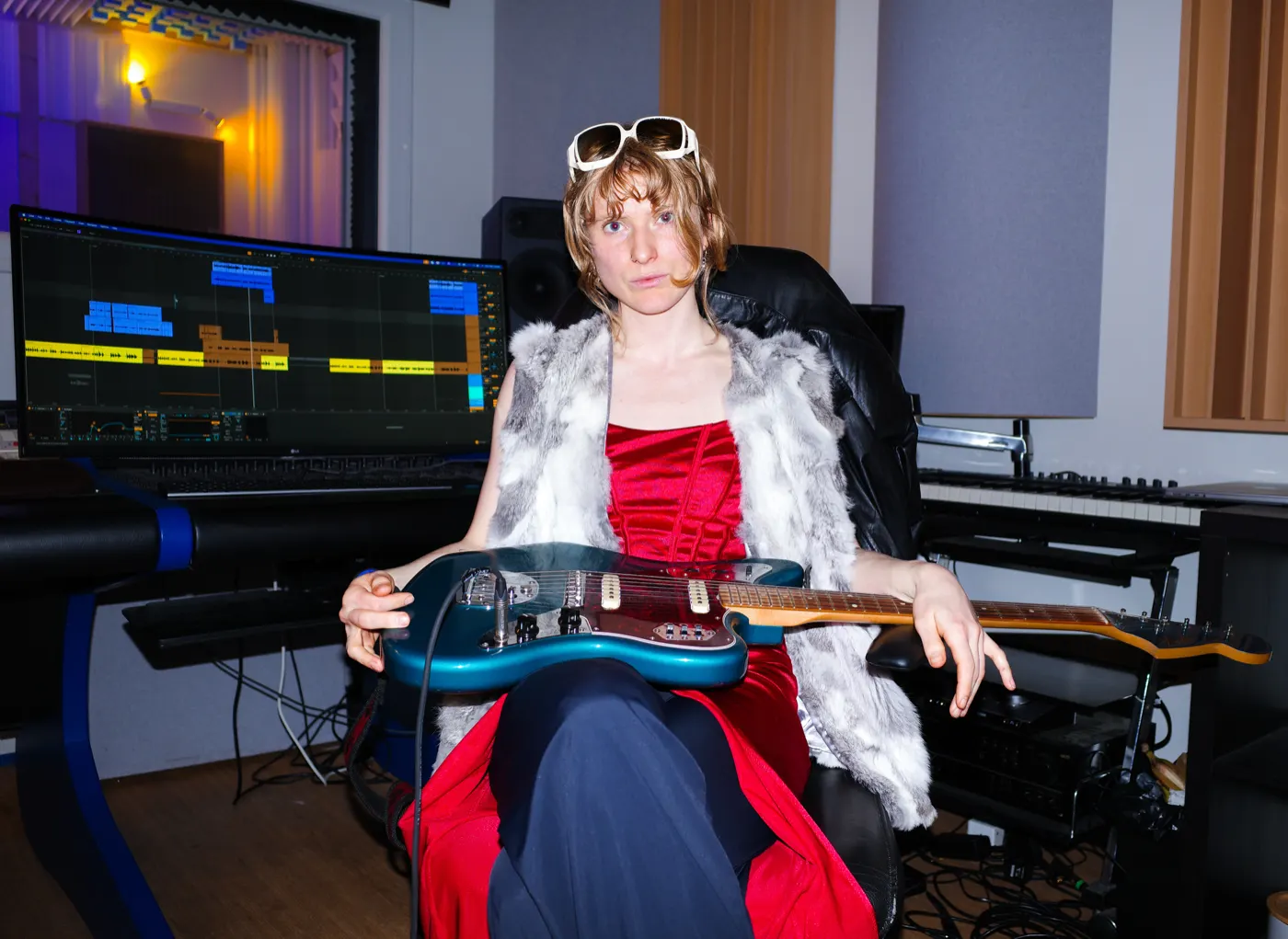 Eva in a red dress and fur vest with an electric guitar, in front of a session in Ableton Live